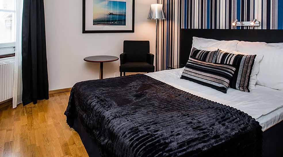 Standard dobbeltværelse med dobbeltseng, bord og lænestol samt stribet tapet hos Quality Hotel Statt i Hudiksvall